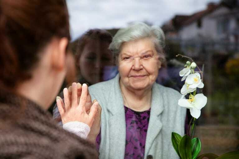Ältere Dame steht hinter Fenster