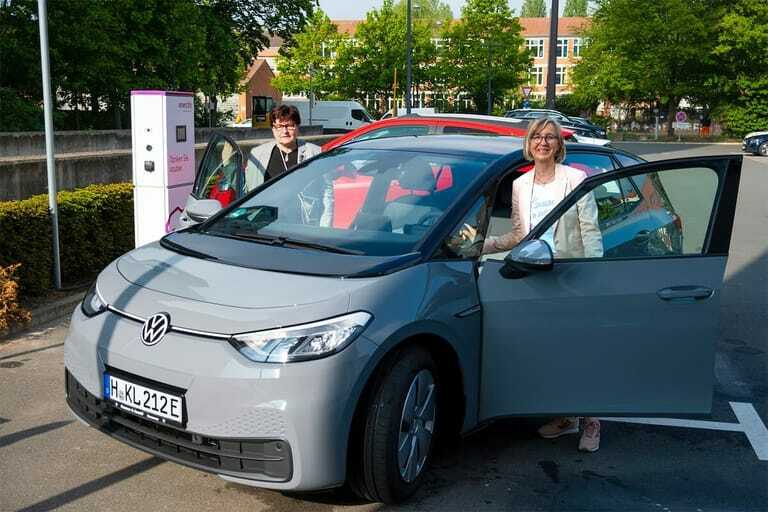 Frau Schweinebraten und Frau Schulte an jeweils einer Vordertür eines Elektroautos.